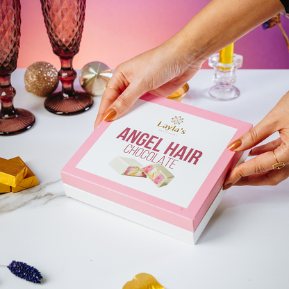 Hand holding a box of Layla's Angel Hair Chocolate with decorative items in the background.