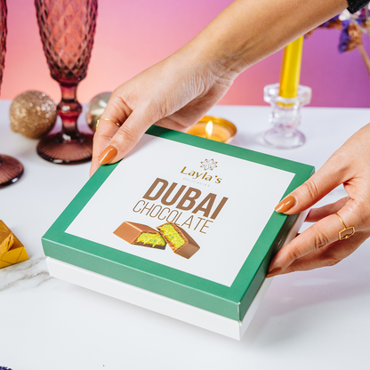 Hand holding a box of Layla's Dubai Chocolate on a decorative table.