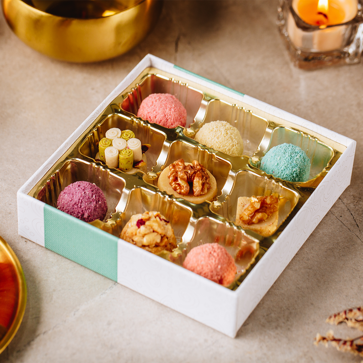 Assorted handmade pastries in a decorative premium gift box on a textured surface with a candle in the background.
