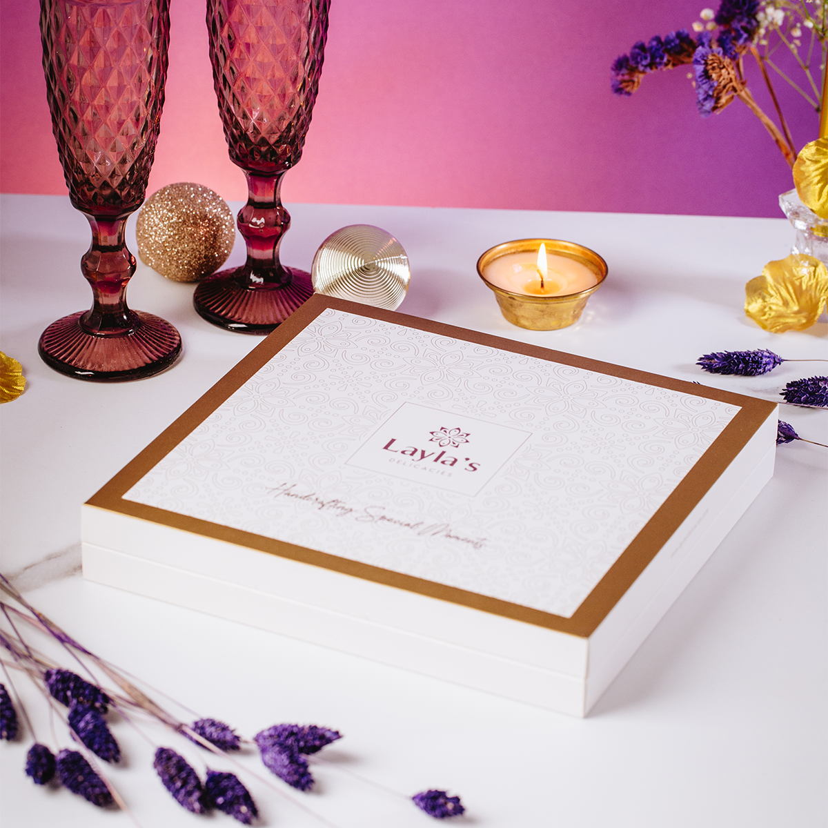 Layla's Delicacies valentine's chocolate gift box with gold border featuring 'Layla's' branding, surrounded by decorative items on a white surface
