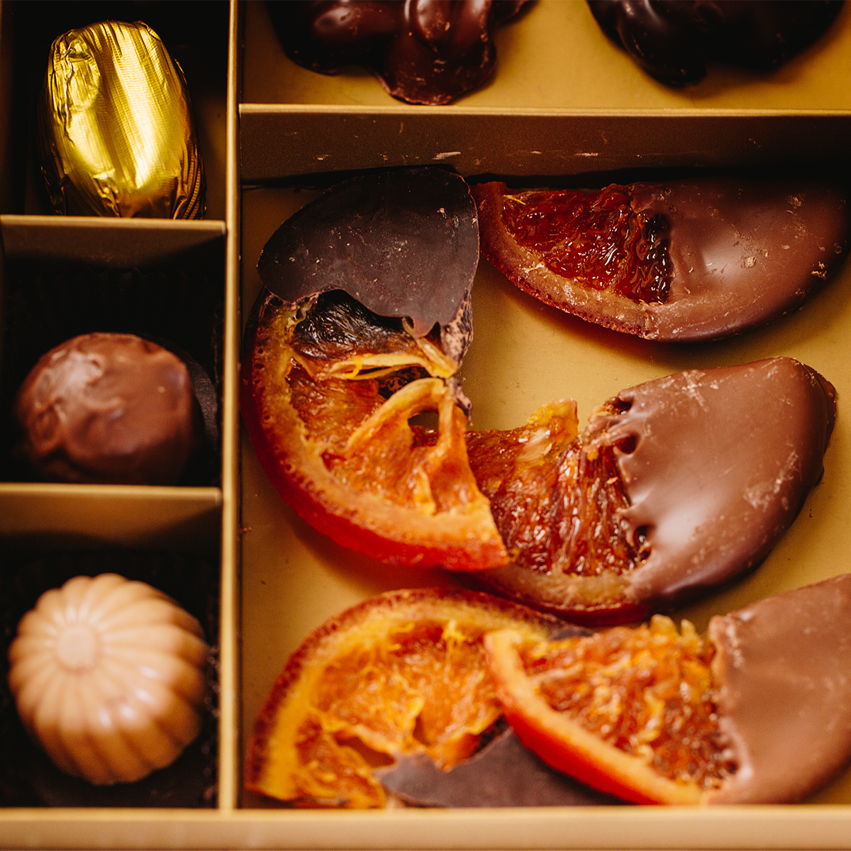 Assorted chocolates including dried fruit and chocolate-covered oranges in a box.
