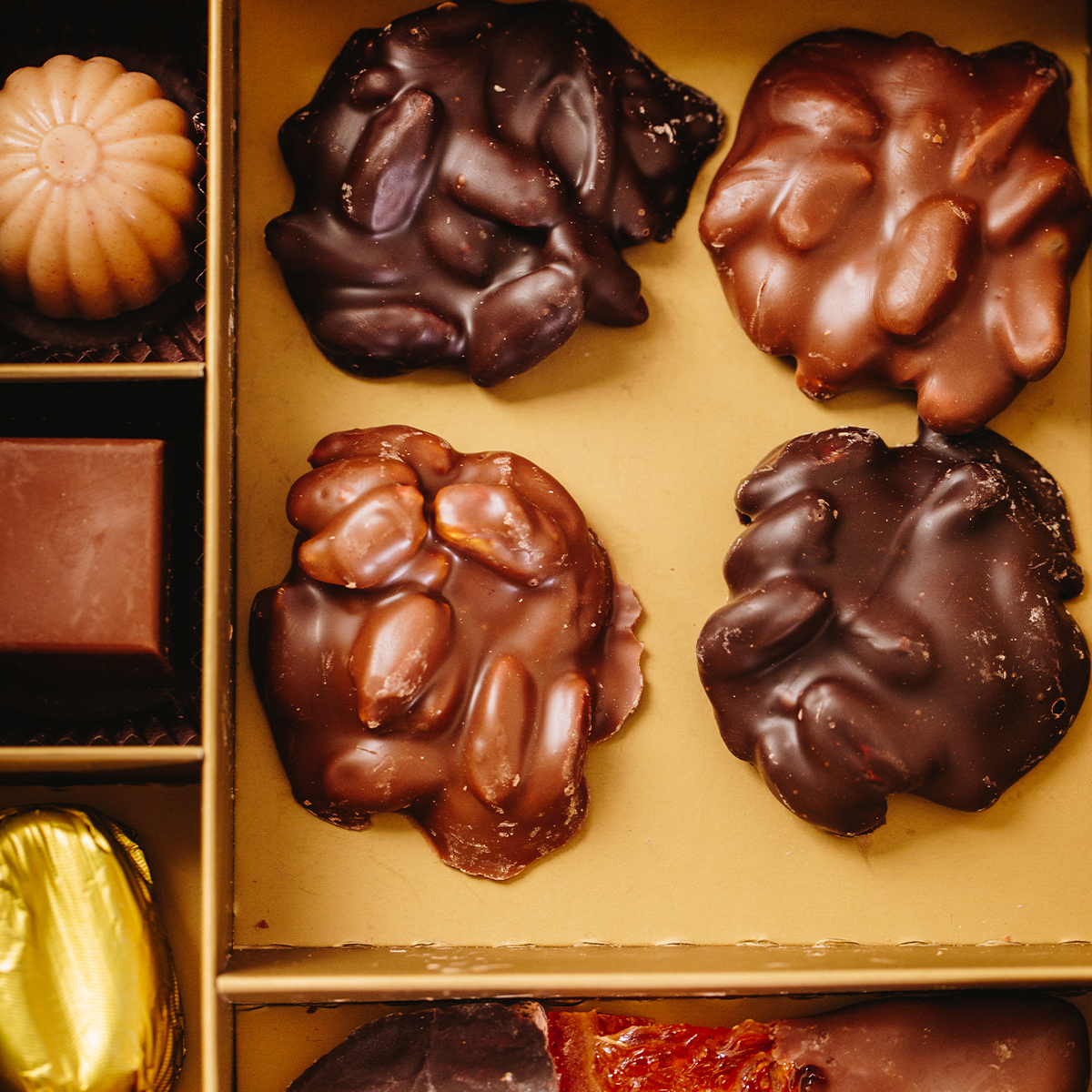 Assorted chocolates including dark pistachio roche and milky pistachio roche pieces with nuts on a gold tray.