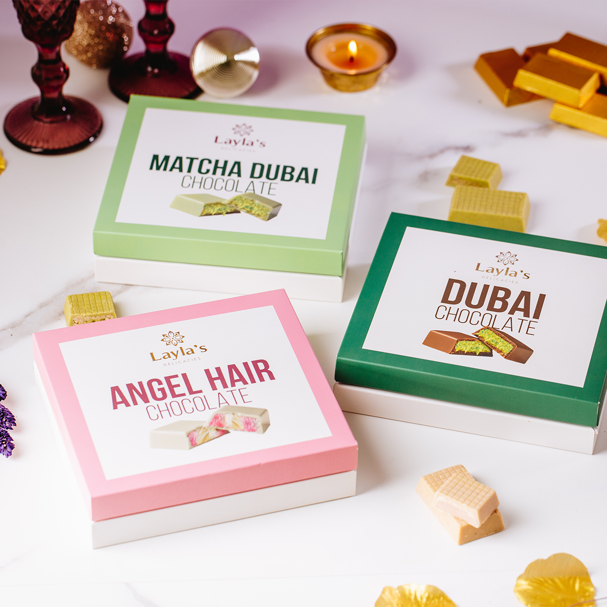 Three boxes of Layla's chocolate for valentine's day gifts, including Matcha Dubai, Dubai chocolate Angel Hair, on a white surface with some chocolate pieces around.