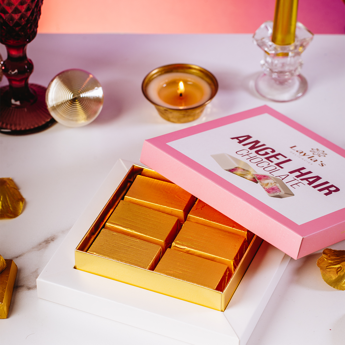 Box of gold chocolate bars with a pink box labeled 'Angel Hair Chocolate' on a decorative table.